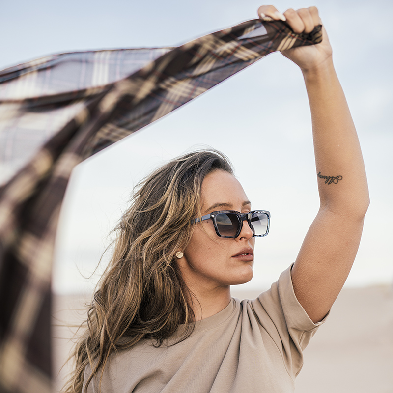 woman wearing sunglasses holding a scarf on the beach